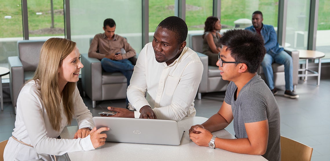 Un groupe d’étudiants est assis autour d’une table et regarde un ordinateur portable.