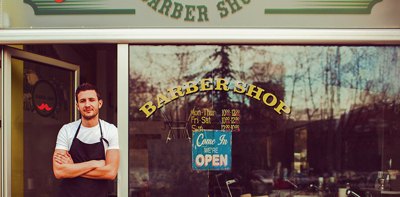 a proud barber shop store owner standing in front of his business