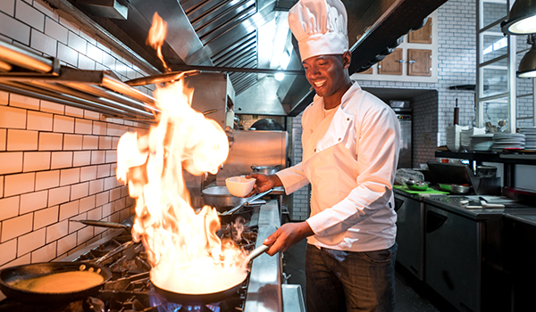 un chef heureux cuisinant dans une cuisine avec de multiples casseroles et poêles remplies de nourriture