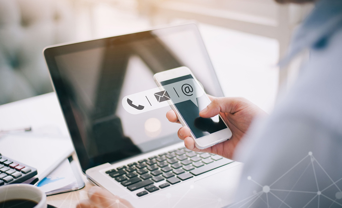 Photo: Man at computer with phone in hand. Email, phone and social media icons visible on screen.