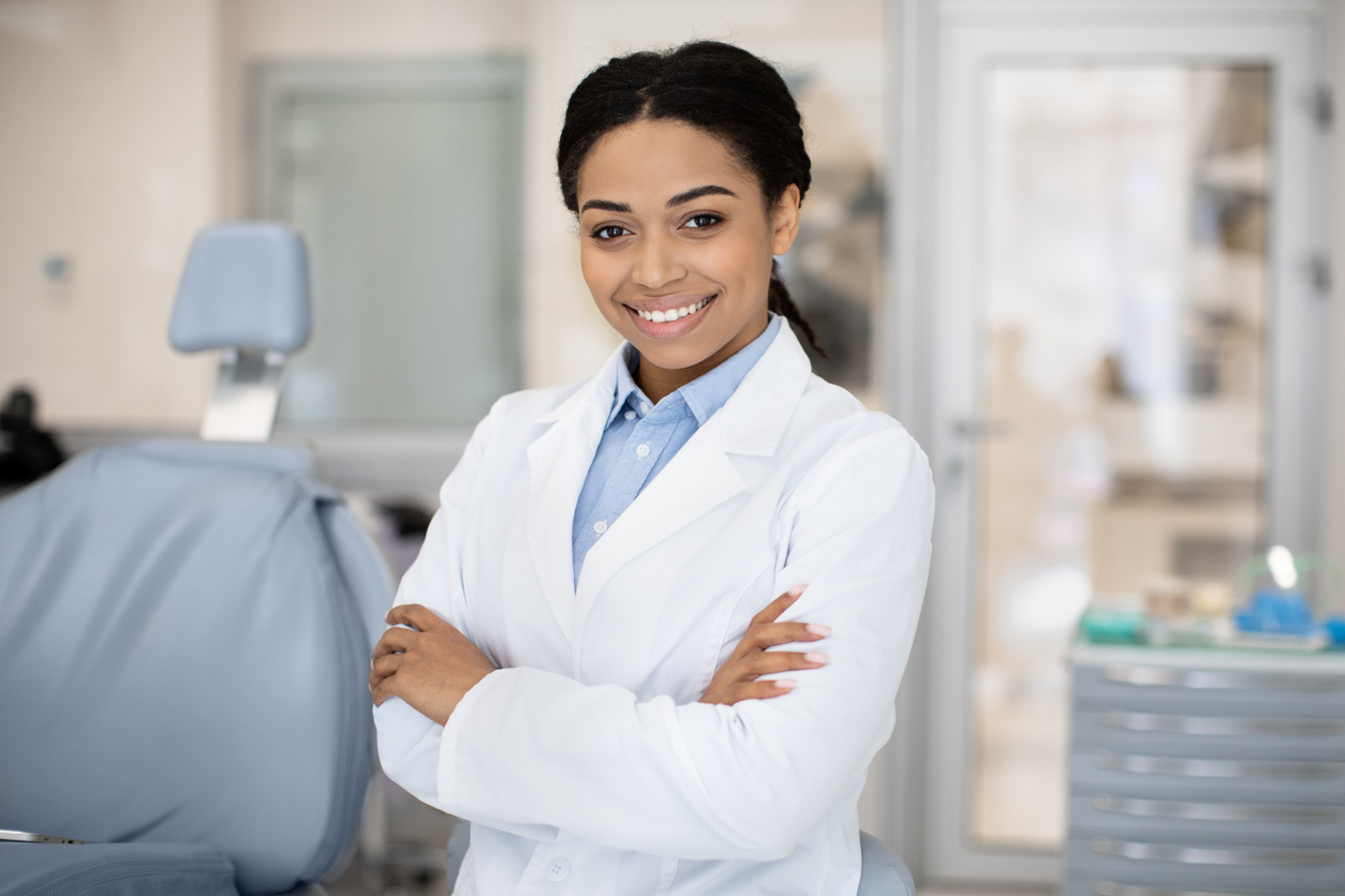 The dentist is standing in their office, smiling.