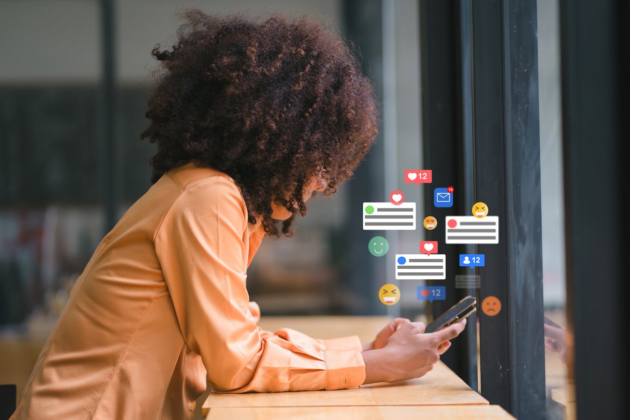 Professional Use of Social Media. Photo of woman sitting and looking at her cell phone screen. Comment bubbles and emojis are depicted above the screen.