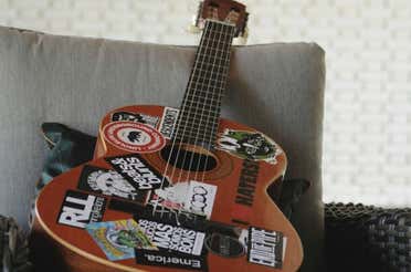 A brown guitar with a lot of stickers on its body placed on top of a sofa.