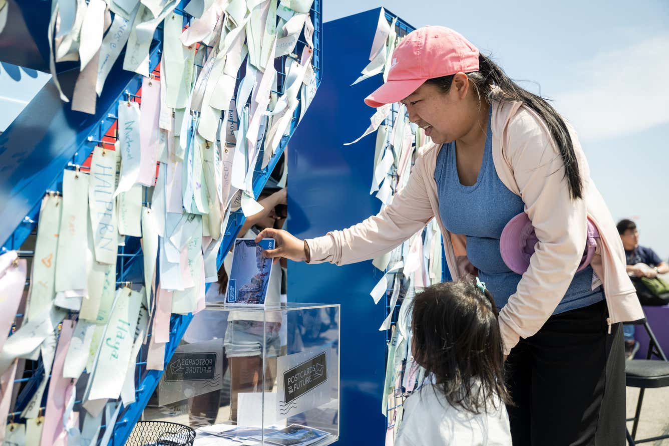 A woman and a child examine a wall covered in colorful notes and messages, engaged in thoughtful discussion.