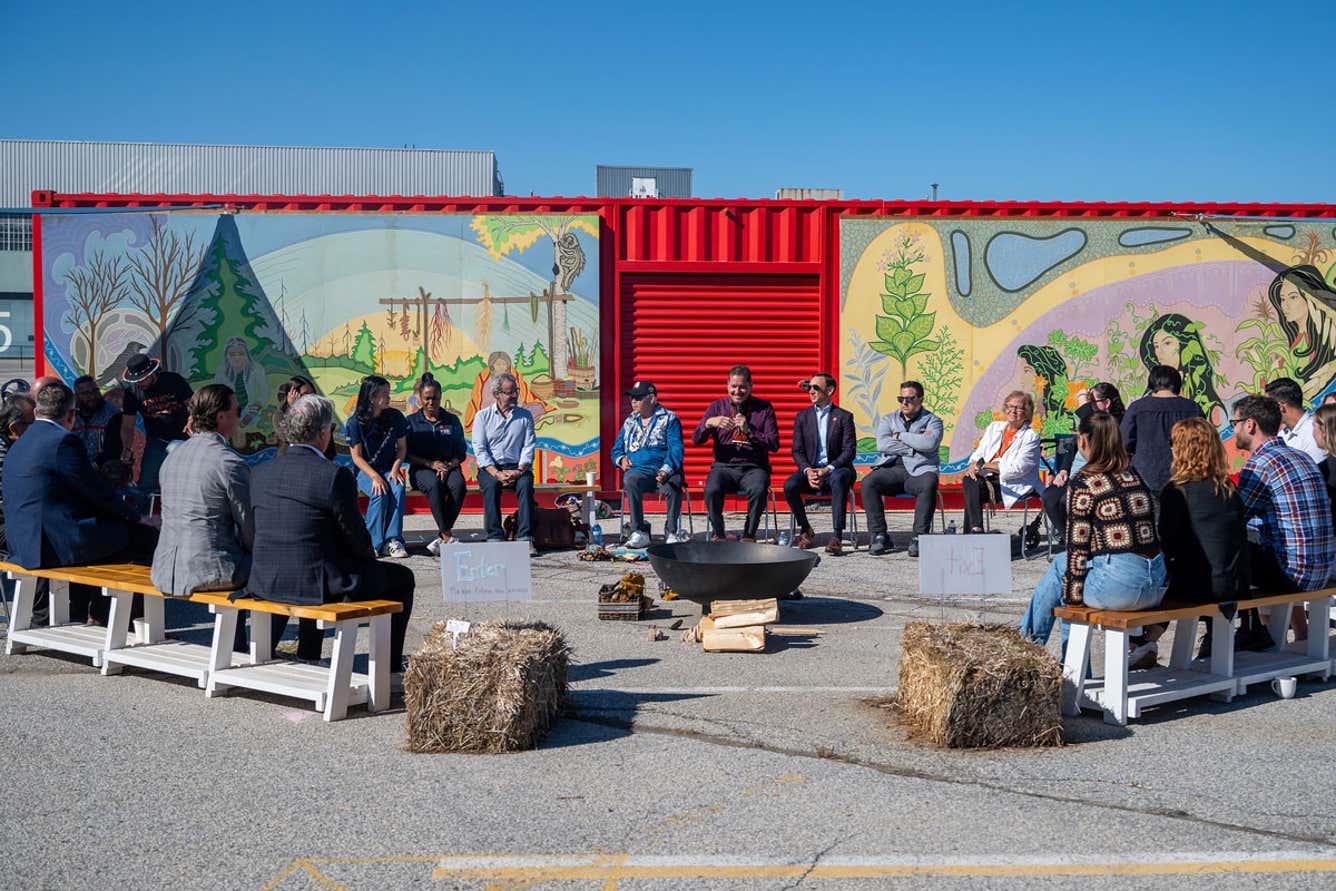 A diverse group of people seated on benches, enjoying a vibrant mural in the background.