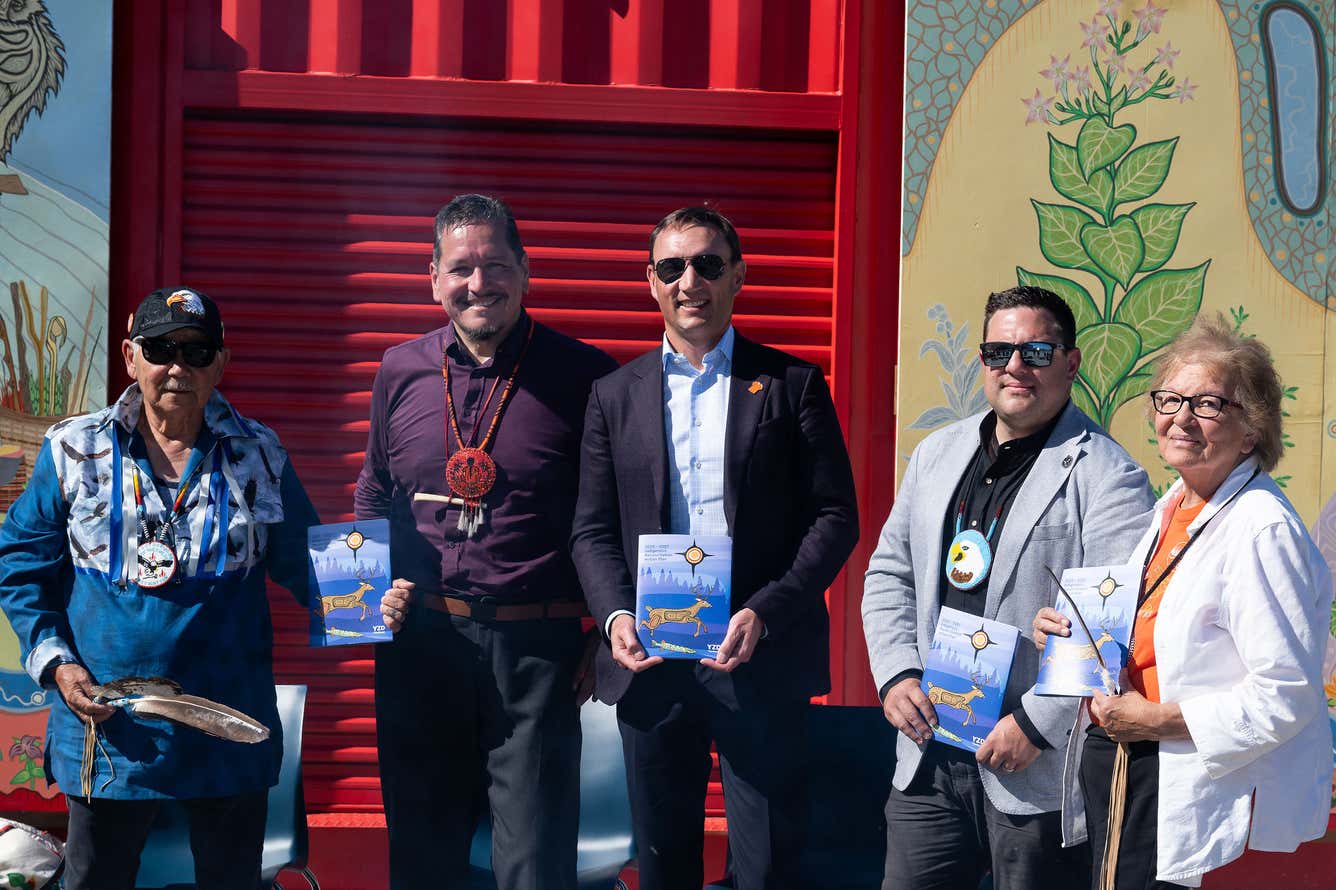 Four individuals stand in front of a red building, each holding a book and smiling at the camera.