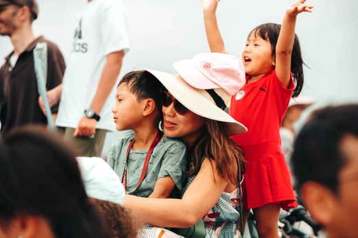 A woman stands with two children in a bustling crowd, all three looking engaged and interacting with their surroundings.